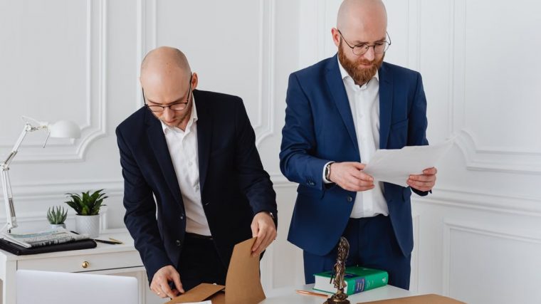Two business professionals in corporate attire reviewing documents in a modern office setting.